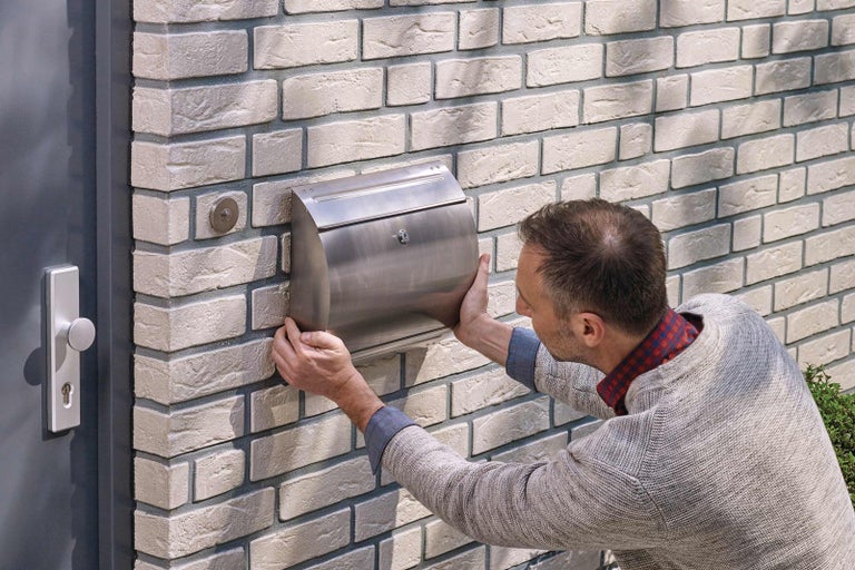 Muž montuje nerezovou poštovní schránku na cihlovou zeď