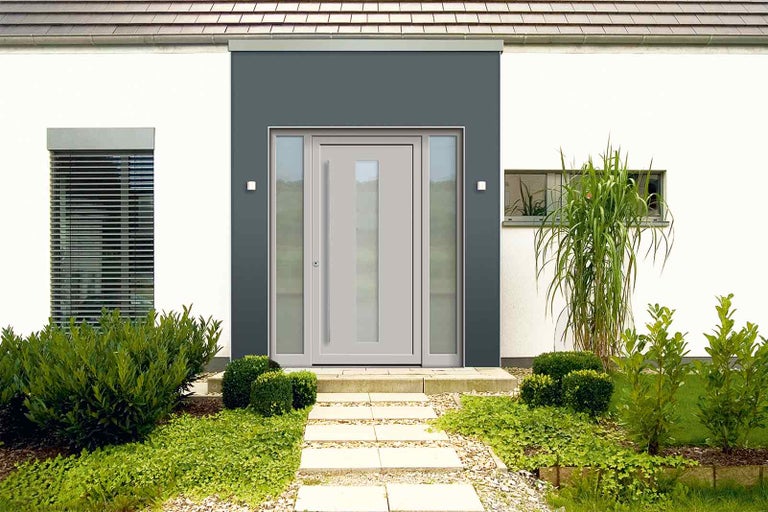 Fasáda domu se vstupními dveřmi se skleněnou vložkou a bočními díly, obklopená zelenými rostlinami.