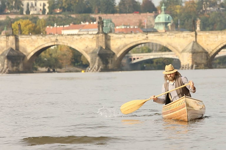 Muž pádluje na kánoi na řece před Karlovým mostem