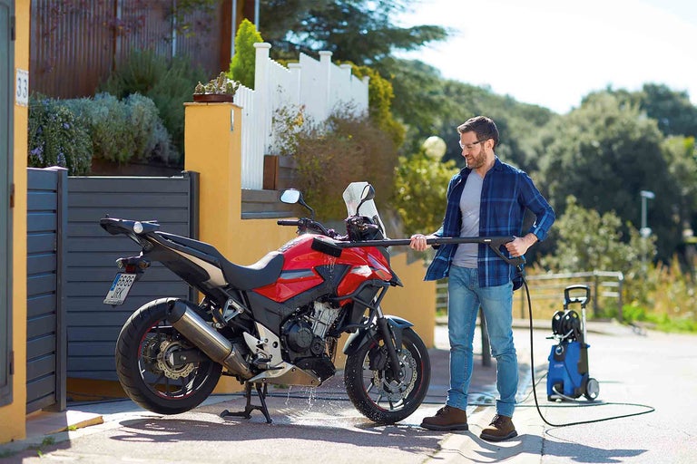 Muž čistí motorku vysokotlakým čističem venku.