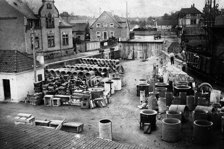 Historická fotografie skladovaných trubek a stavebních prvků na staveništi