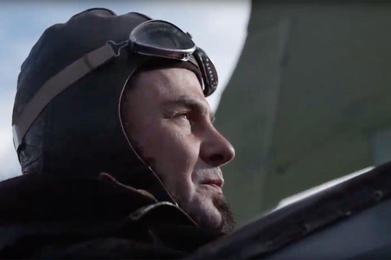 Muž s leteckou kuklou a brýlemi se dívá do dálky