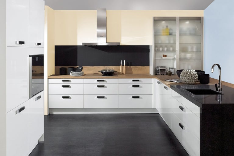 Světlá kuchyně s bílými skříňkami, tmavými pracovními deskami a nerezovým odsavačem par.