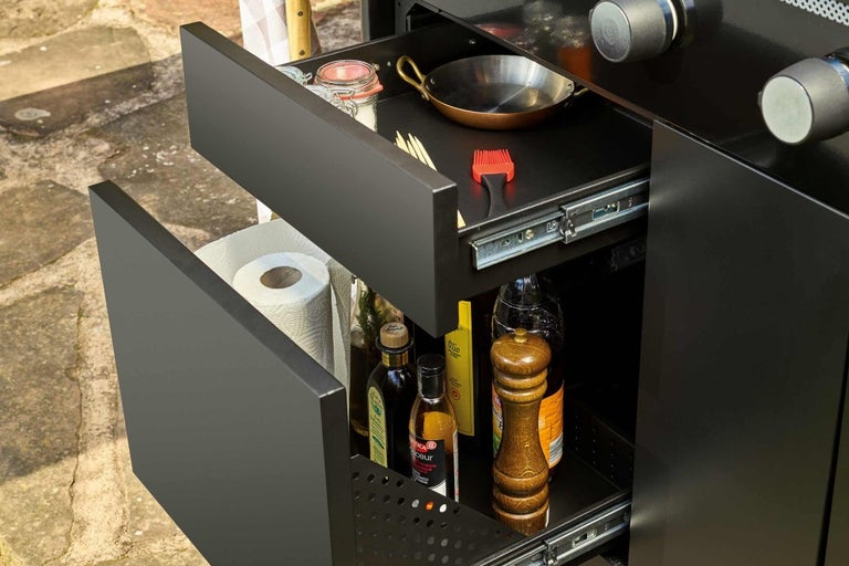 Otevřené zásuvky černé venkovní kuchyně s kuchyňským náčiním a potravinami