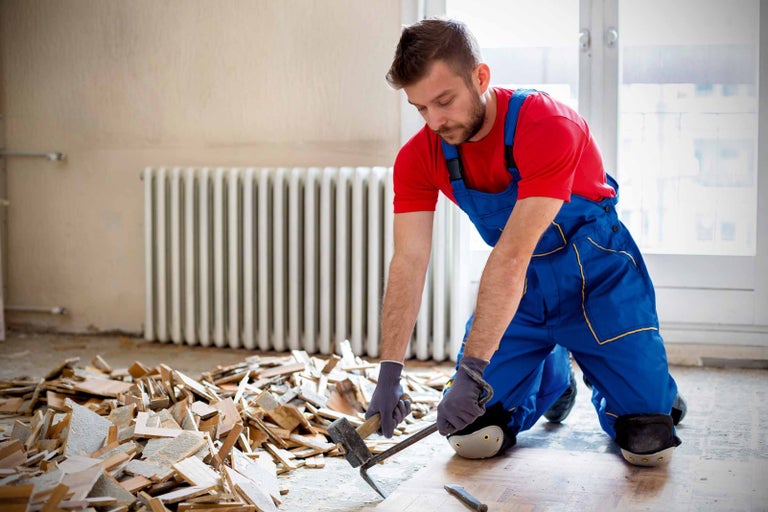 Řemeslník odstraňuje dřevěnou podlahu kladivem a páčidlem