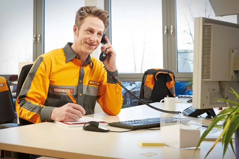 Zaměstnanec společnosti Hornbach telefonuje u stolu a dělá si poznámky.