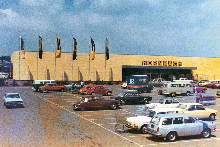 Historická fotografie obchodu Hornbach se stavebninami s parkovištěm a různými auty.