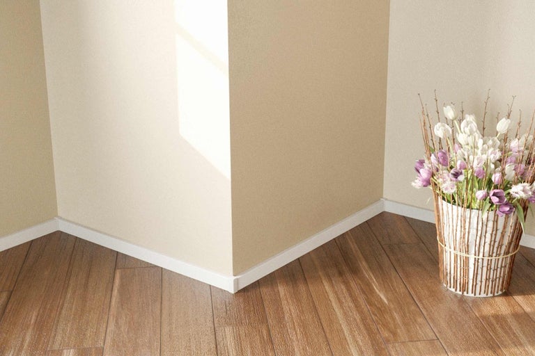 Roh místnosti s dřevěnou podlahou, bílými podlahovými lištami a květinovou výzdobou