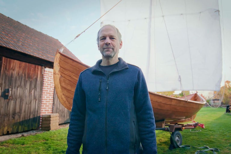 Muž stojí před dřevěnou lodí s plachtou na přívěsu