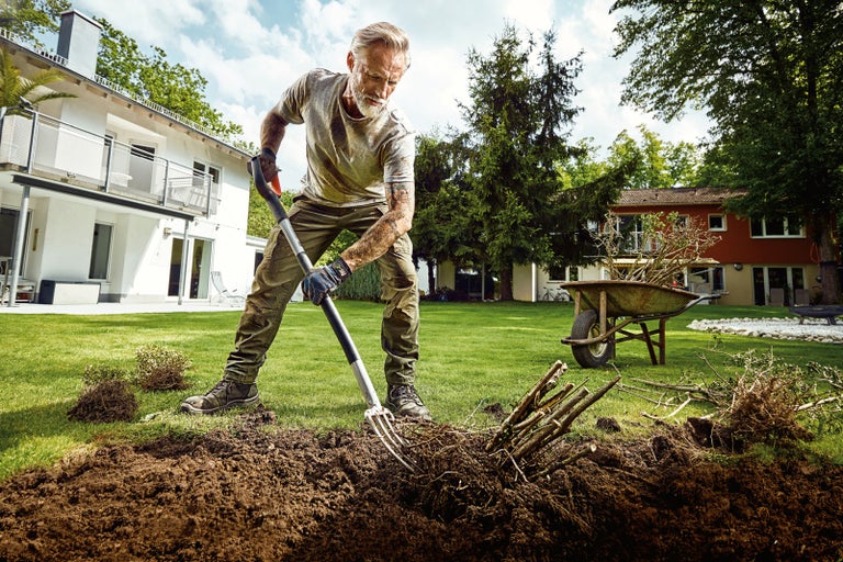 Muž používá rycí vidle pro zahradnické práce na zahradě.