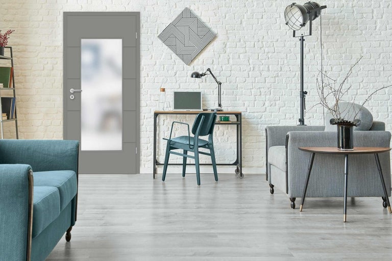 Moderní obývací pokoj s šedými interiérovými dveřmi, psacím stolem a posezením před bílou cihlovou zdí