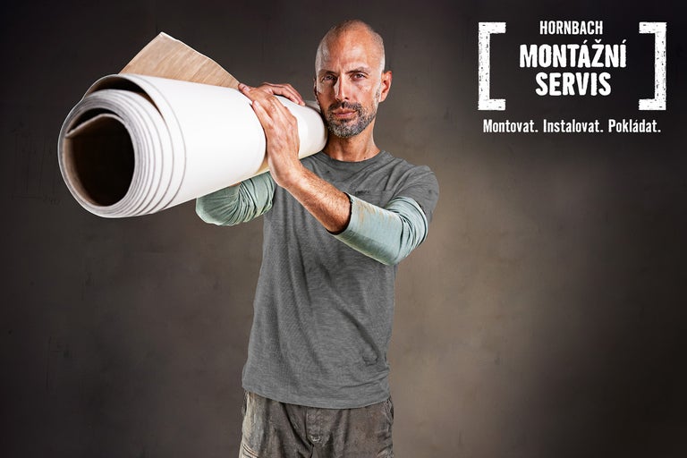 Muž nese na rameni roli podlahové krytiny. Montážní servis Hornbach.
