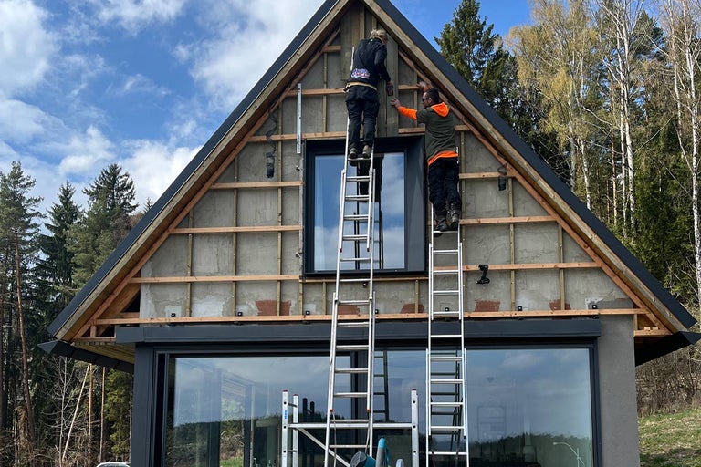 Dva řemeslníci na žebřících montují fasádu na dům.