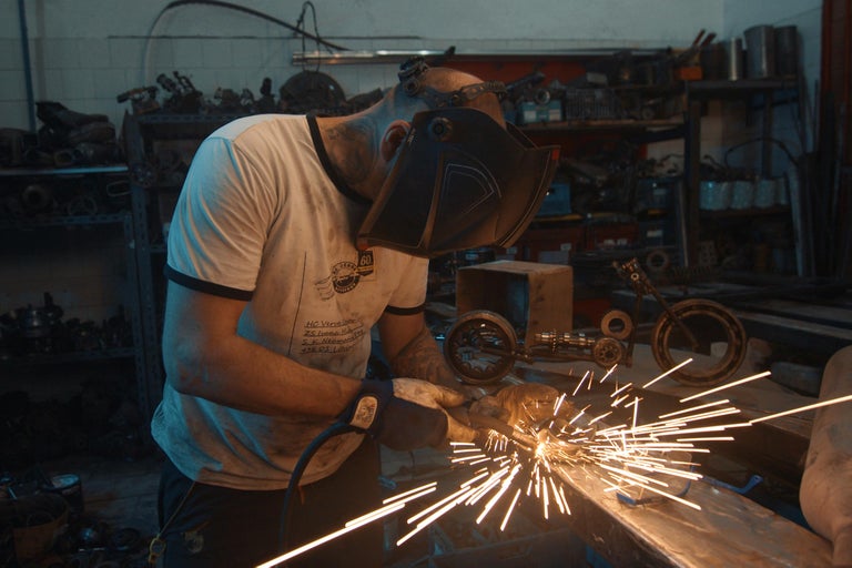 Muž s ochrannou maskou svařuje kov v dílně