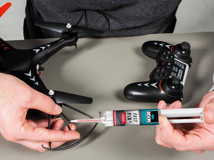 Osoba opravuje dron s lepidlem na plasty Bison vedle dálkového ovládání dronu.