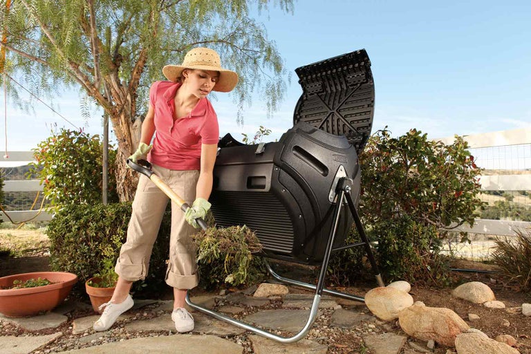 Žena plní kompostovací nádobu na zahradě rýčem.