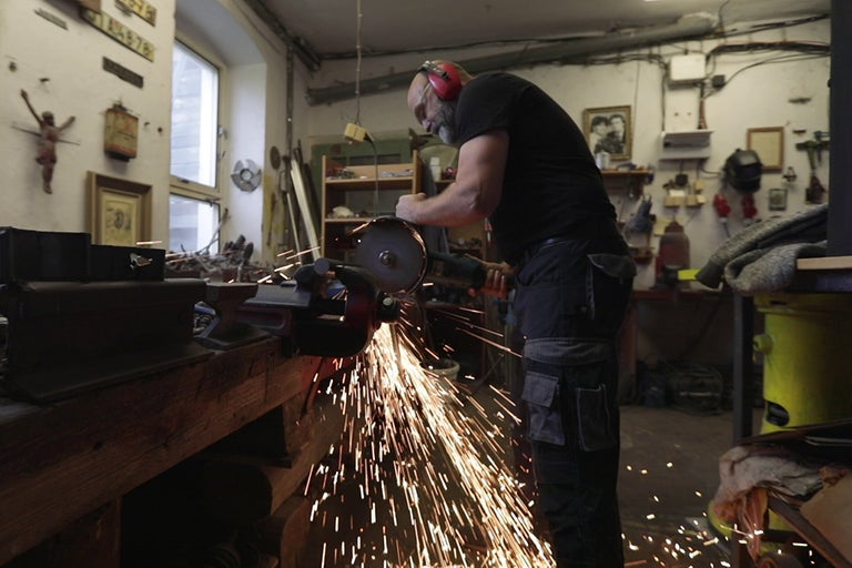 Muž brousí kov úhlovou bruskou v dílně