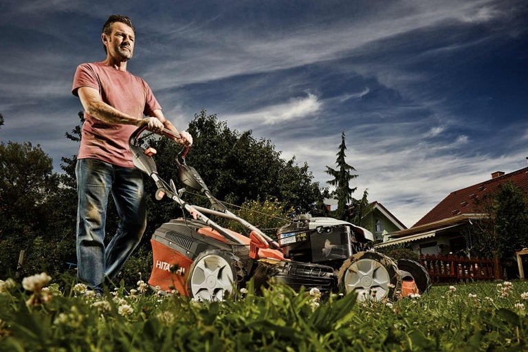 Muž seče trávník sekačkou na trávu na zahradě.