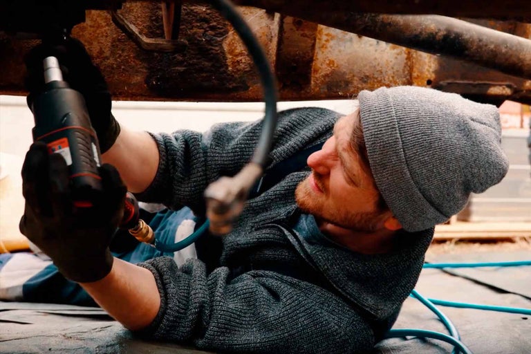 Muž leží pod autem a pracuje s rázovým utahovákem