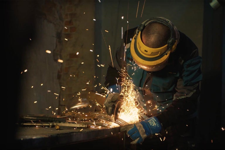 Osoba pracuje s bruskou, létají jiskry, používá přitom ochranné pomůcky.