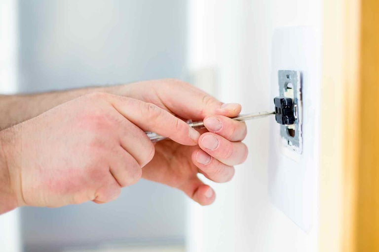 Elektrikář montuje vypínač světla pomocí šroubováku.