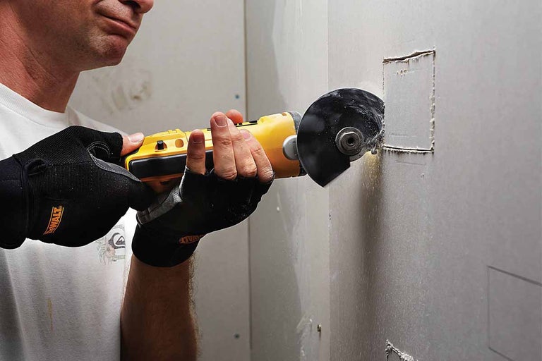 Osoba vyřezává otvor do sádrokartonu pomocí rozbrušovací pily.