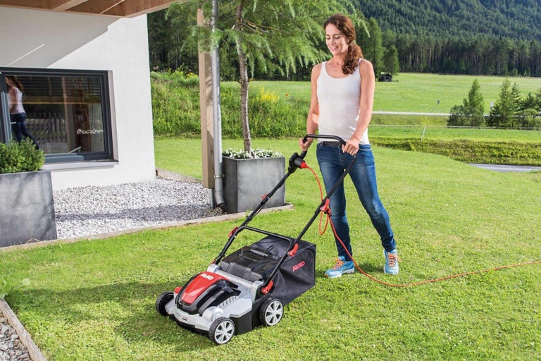 Žena používá sekačku na trávu na zahradě.