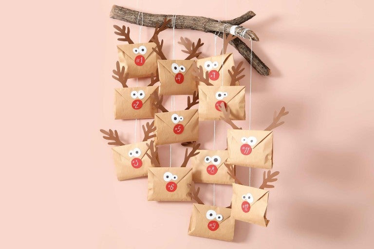 Adventní kalendář s papírovými obálkami, čísly a parohy visícími na větvi