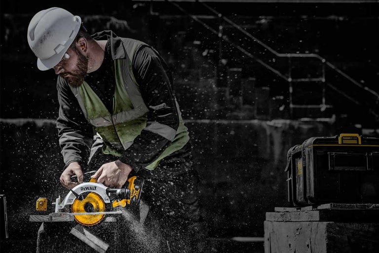 Stavební dělník řeže dřevo ruční kotoučovou pilou DeWalt, v pozadí je box na nářadí.