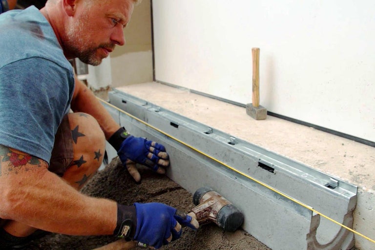 Muž pokládá dlažební kostky pomocí kladiva a vodicí šňůry