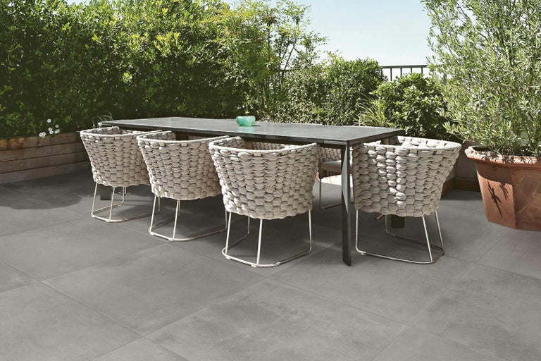 Zahradní sedací souprava s jídelním stolem a proutěnými křesly na šedé terasové podlaze