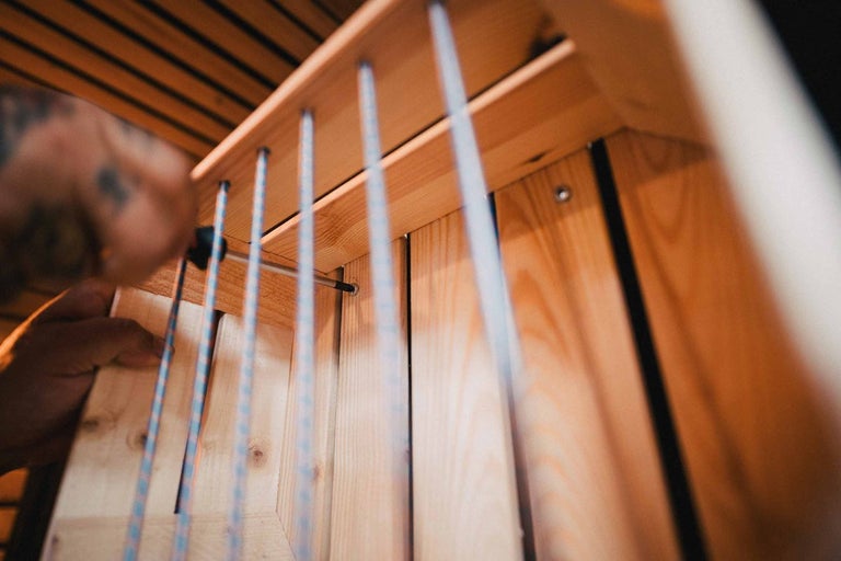 Osoba upevňuje dřevěnou konstrukci pomocí šroubů a lan