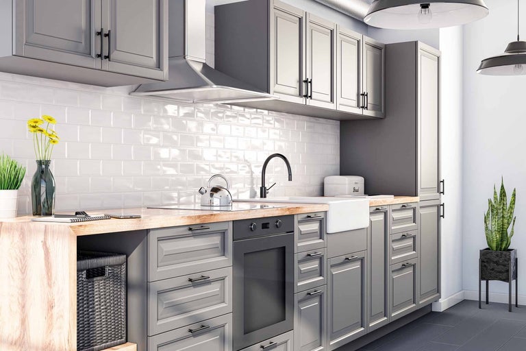 Světlá kuchyně s šedými skříněmi, dřevěnou pracovní deskou a bílými obklady
