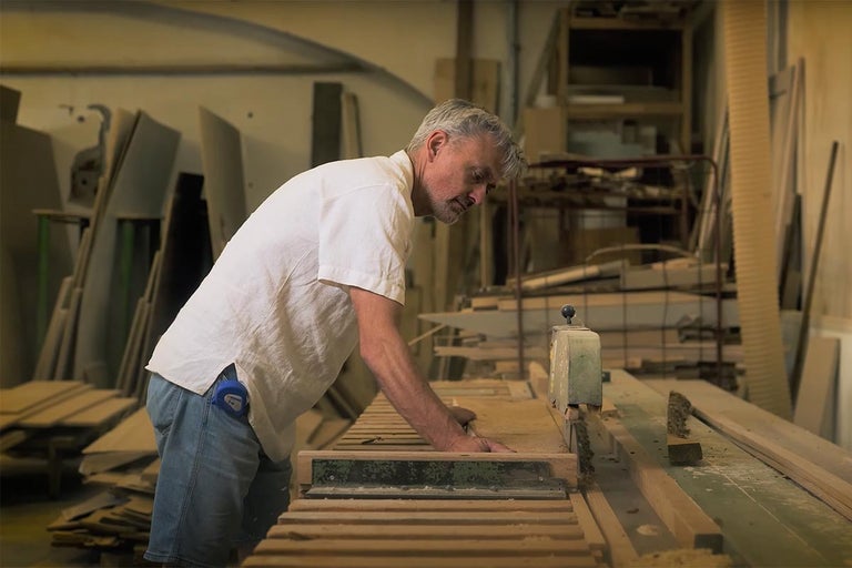 Muž pracuje s kotoučovou pilou ve workshopu s dřevěnými materiály.