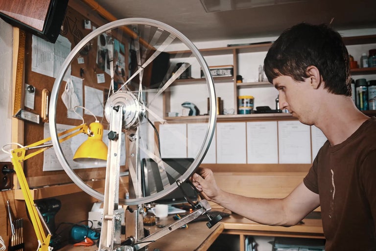 Muž opravuje kolo pomocí vycentrovacího stojanu v dílně.