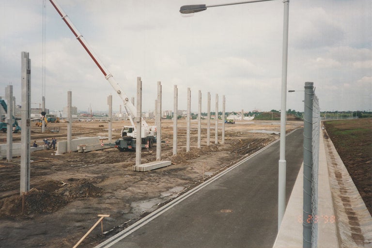 Staveniště s betonovými pilíři, jeřábem a stavebními dělníky