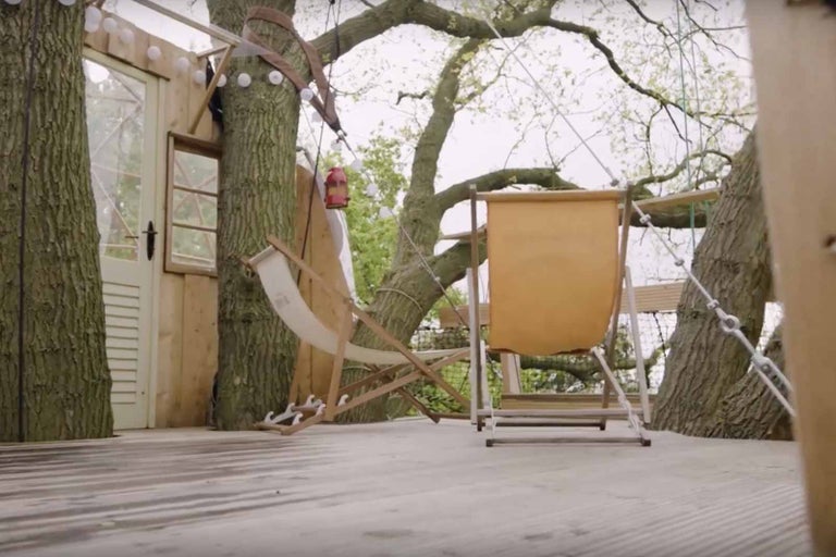 Dům na stromě s dřevěnou terasou a lehátky.