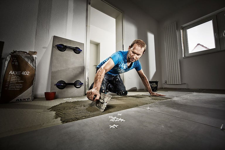 Řemeslník pokládá dlaždice s flexibilním lepidlem Akkit 402 v místnosti