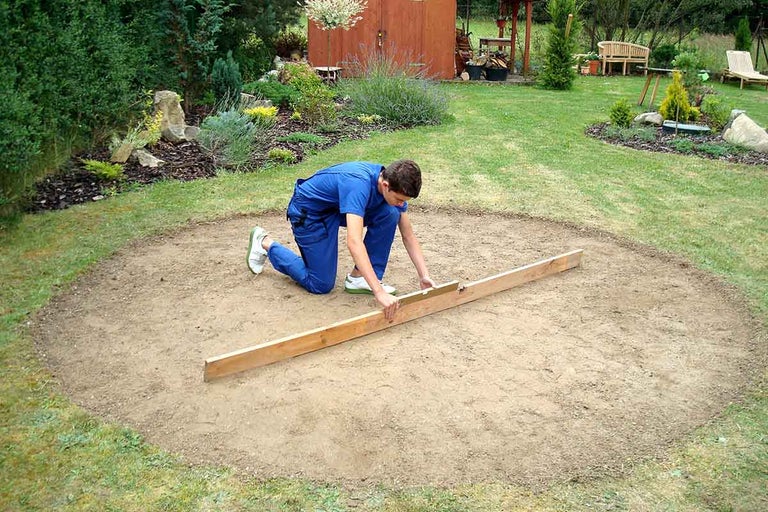 Muž vyrovnává plochu pomocí latě na zahradě