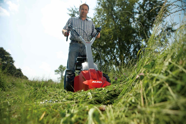 Muž obsluhuje bubnovou sekačku AL-KO při sekání trávy