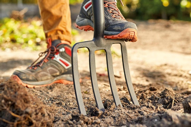 Detailní záběr zahradních vidlí, které se nohou zatlačují do země.