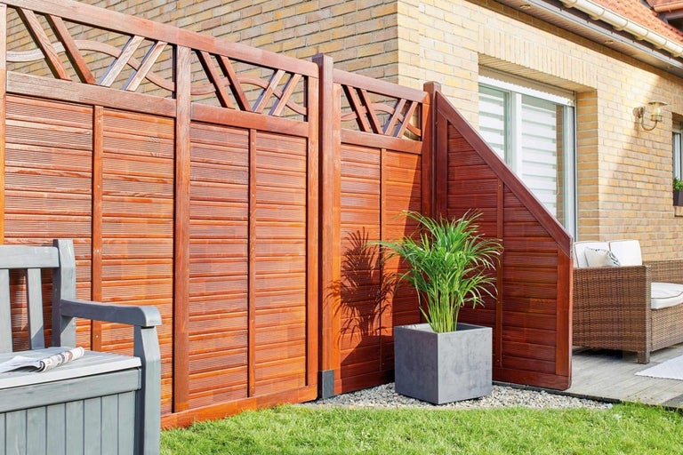 Dřevěný plot s dekorativním designem a květináčem na zahradě