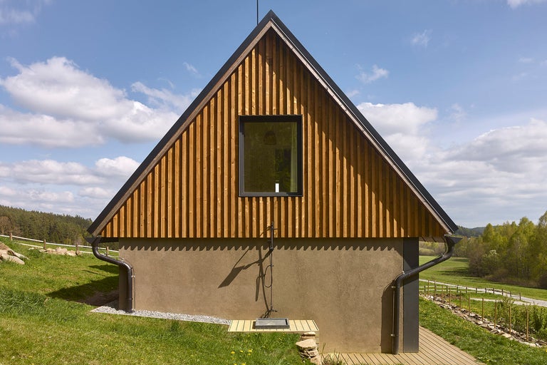 Pohled na dům s dřevěným obkladem, oknem a venkovní sprchou