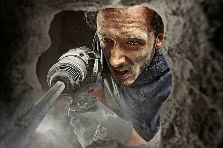 Muž vrtá sbíjecím kladivem betonovou zeď