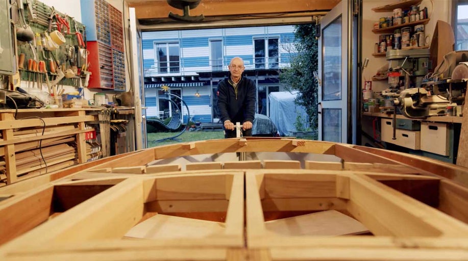 Muž staví dřevěnou loď v dílně.