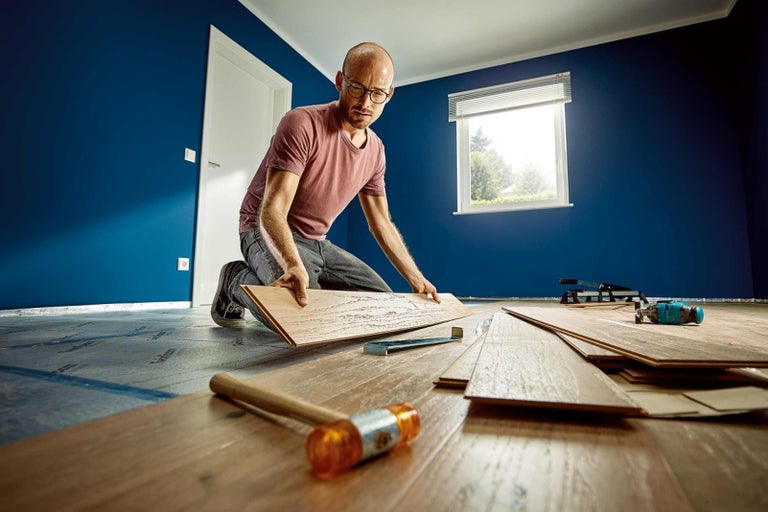 Muž pokládá laminátovou podlahu v místnosti s nářadím.