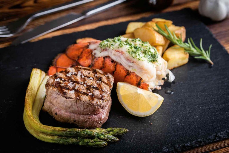 Surf and Turf talíř se steakem, humrem, bramborami a zeleninou na tmavém talíři