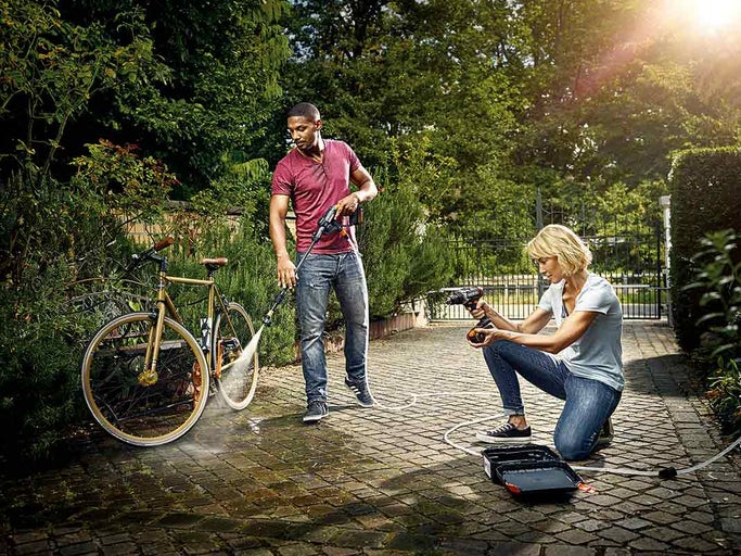 Muž čistí kolo tlakovou myčkou, zatímco žena poblíž používá vrtačku.