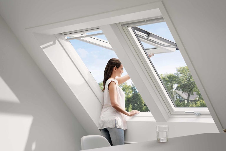 Žena otevírá střešní okno ve světlé místnosti.