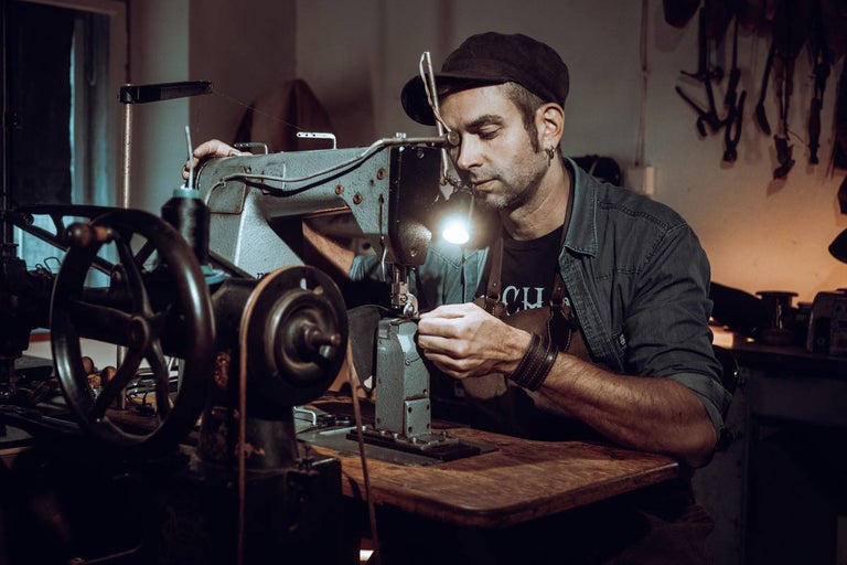 Muž pracuje se šicím strojem na dřevěném stole.
